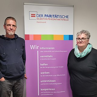 Auf dem Bild sind zwei Personen mit dem Roll Up von der Paritätischen Selbshilfekontaktstelle