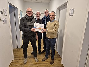 Vier Männer, linke übergibt Mappe an rechten