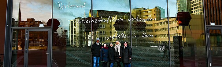 Team der Selbsthilfe-Kontaktstelle: vier Personen, Schriftzug "Dortmund gemeinschaftlich verbunden, weltoffen im Kern"
